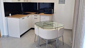 A modern kitchen with white cabinets, a black countertop, a glass dining table, and a built-in microwave. - Apartments 4 You (Novalja)