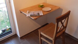 A small dining area with a wooden table, a chair, a clock, and a newspaper on the table. - Atelier IM Stadtgarten - Direkt in Rottweil Schwarzwald Bodensee (Rottweil)