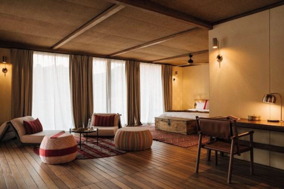 A modern hotel room with a wooden floor, a sofa, a chair, a small table, and a desk area.