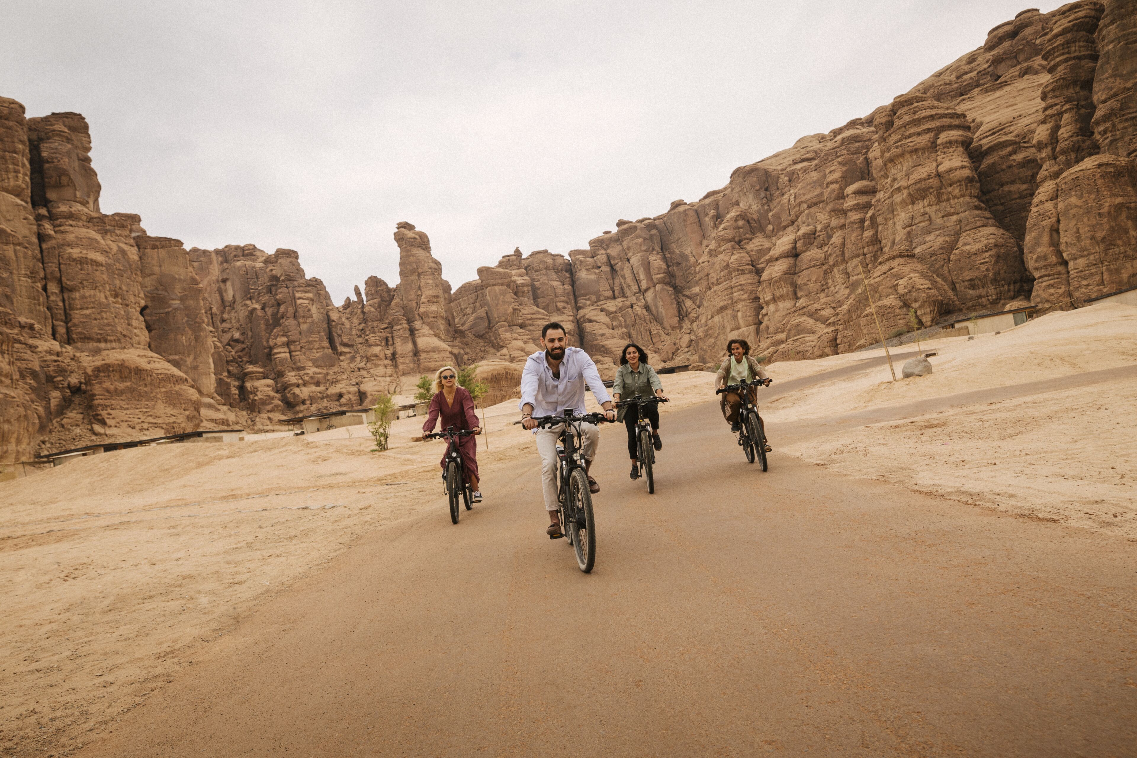 Un grupo de personas pedaleando en bicicleta por un camino de tierra en un paisaje desértico con acantilados rocosos.