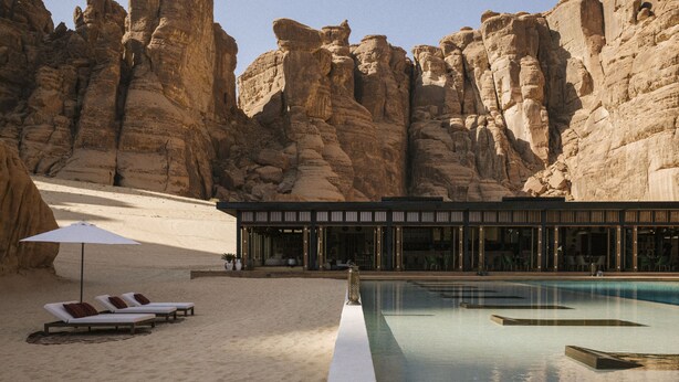 Zona de piscina con sillones de descanso y un edificio de diseño moderno.