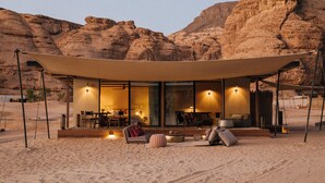 Un resort en el desierto con una zona de estar cubierta al aire libre, un espacio para comer y vistas del paisaje rocoso circundante.