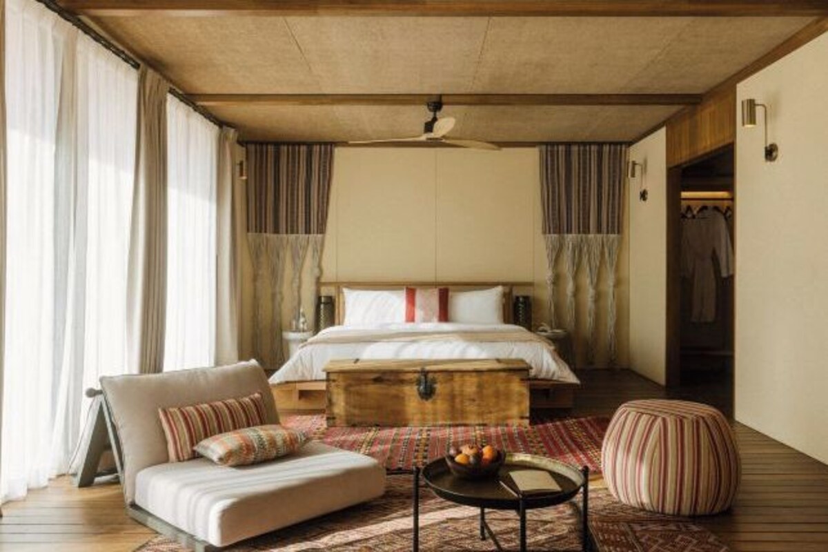 Een slaapkamer met een bed, een bank, een houten kist en een ronde tafel met fruit.