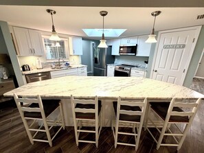 A modern kitchen with a large island, white cabinetry, and a skylight.