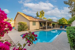 A house with a swimming pool, a covered patio, and a garden with bougainvillea flowers.