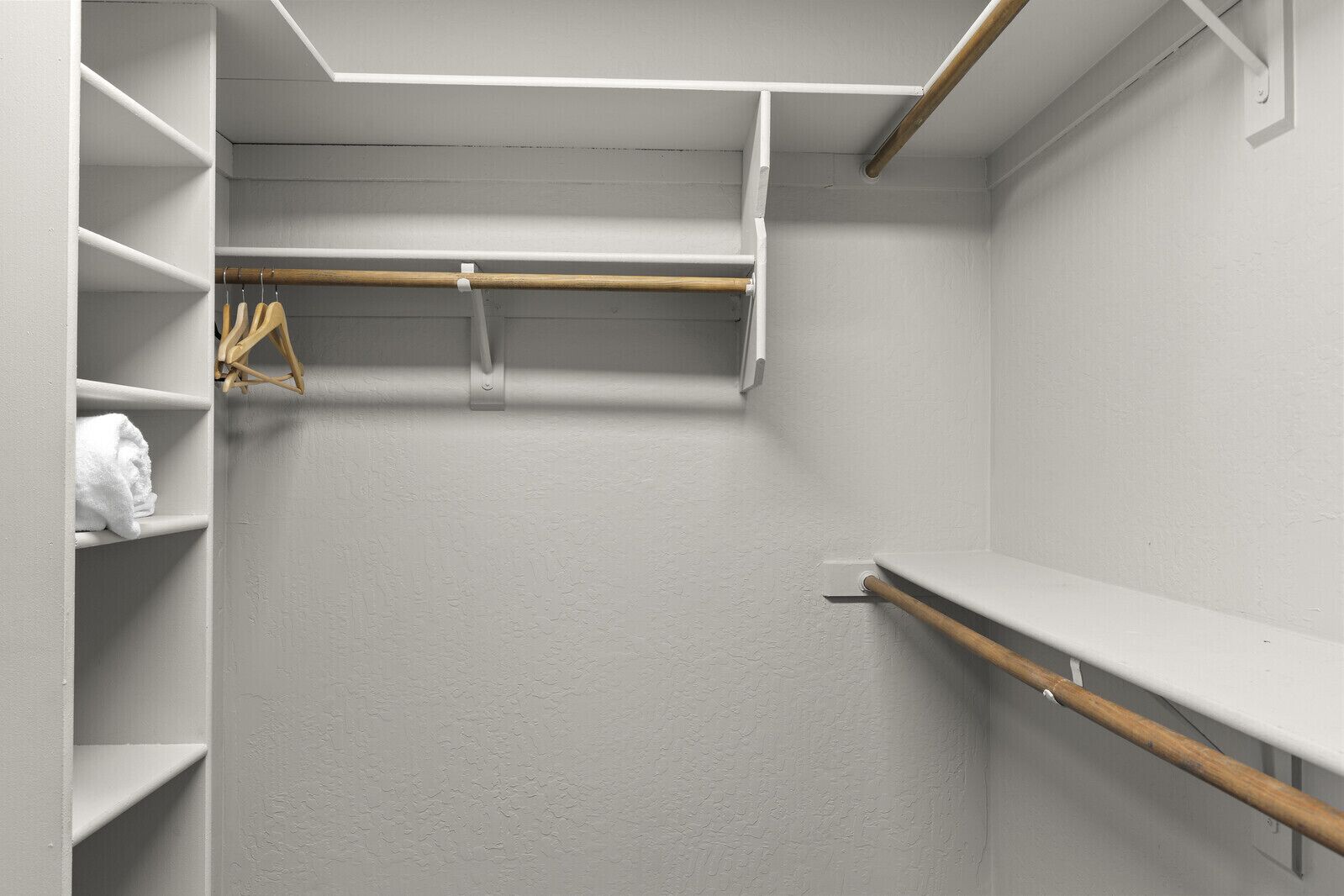 Um closet amplo com paredes brancas, prateleiras de madeira e uma barra para pendurar roupas.