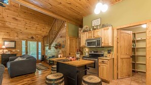A rustic cabin interior with wooden floors, a kitchen with wooden cabinets, a dining area with a bar, and a staircase. - THREE BEARS CABIN, PRIVATE MOUNTAIN GETAWAY (Sautee Nacoochee)