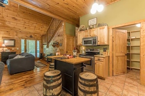 A rustic cabin interior with wooden floors, a kitchen with wooden cabinets, a dining area with a bar, and a staircase. - THREE BEARS CABIN, PRIVATE MOUNTAIN GETAWAY (Sautee Nacoochee)