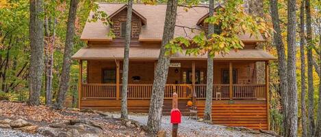 A log cabin with a porch, surrounded by trees and a gravel path.