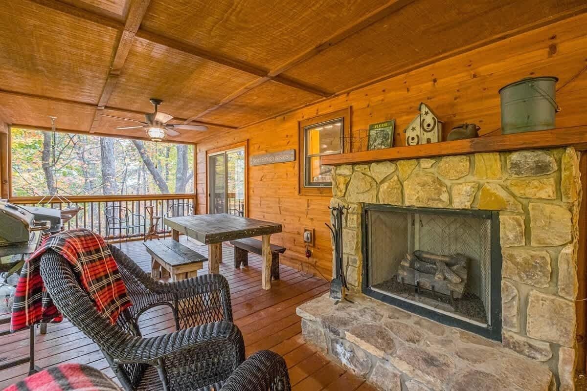 A wooden deck with a stone fireplace, wicker chairs, a table, and a ceiling fan.