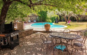 Un jardin avec un barbecue, une table ronde entourée de chaises, une piscine et un grand vase.