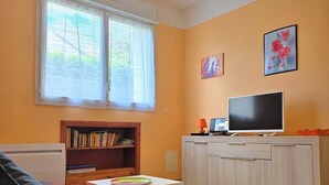 Una sala de estar con sofá, televisión, estantería y ventana con persianas.