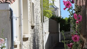 Una calle estrecha bordeada por edificios, cielo despejado y plantas con flores.