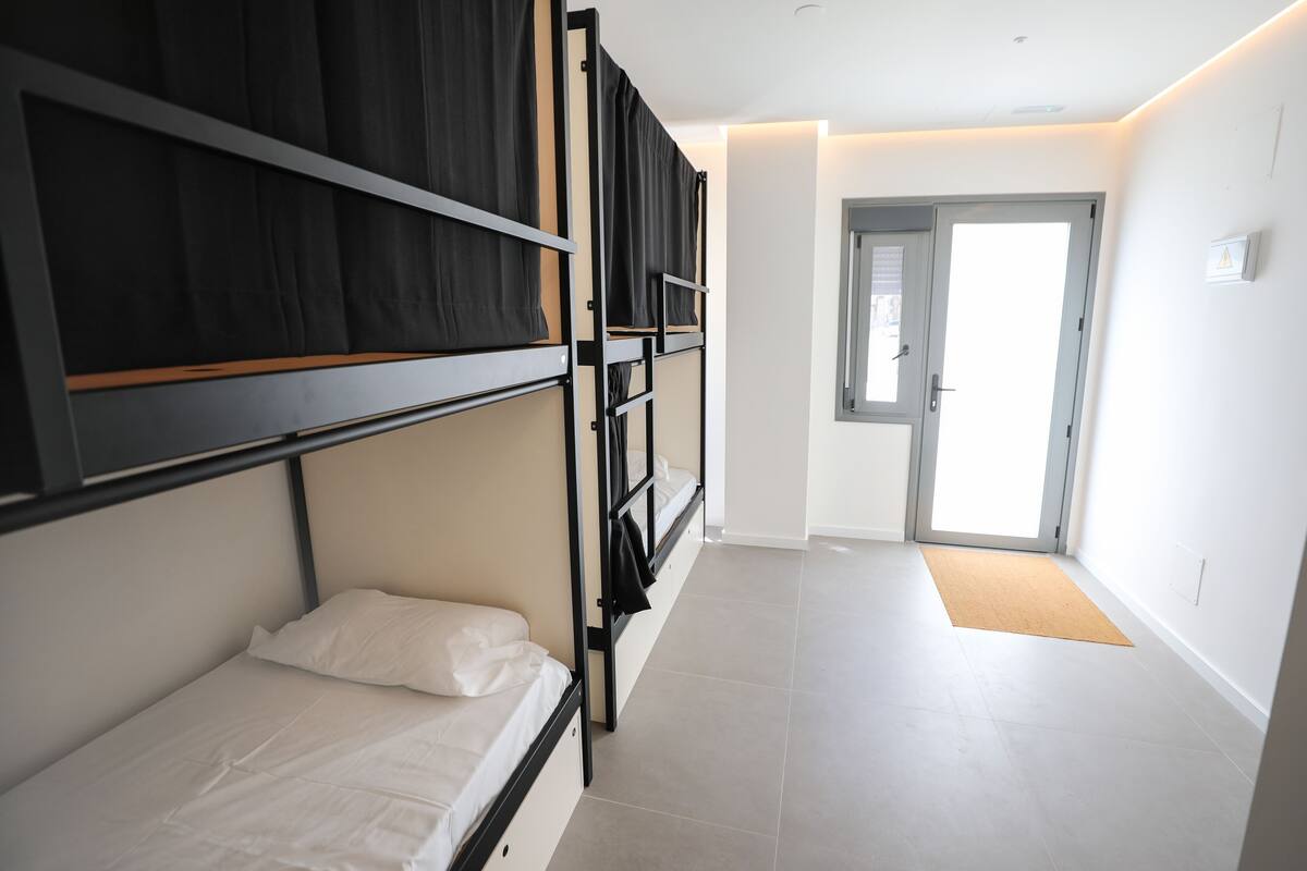 Una habitación de hotel moderna con literas, una puerta que da a un balcón y un suelo de baldosas de color claro.