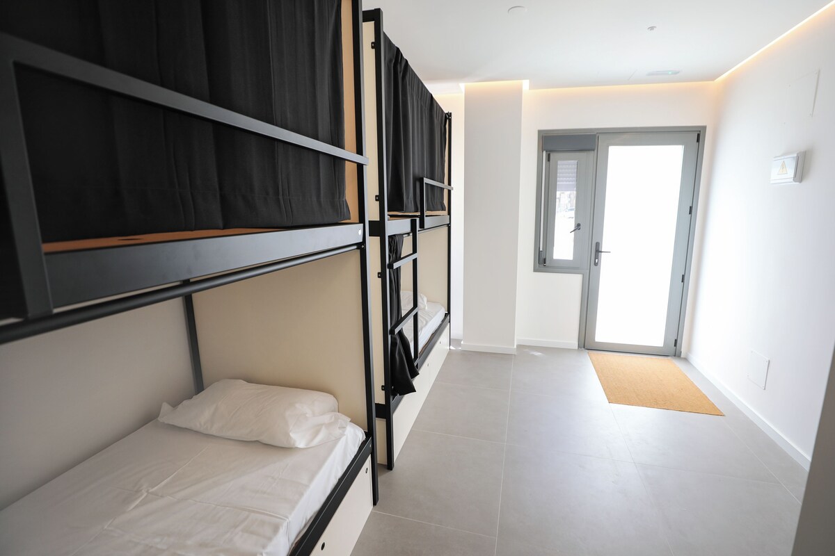 Una habitación de hotel moderna con literas, una puerta que da a un balcón y un suelo de baldosas de color claro.