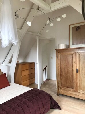 Ein Schlafzimmer mit Bett, einem hölzernen Schminktisch, einem Kleiderschrank und einer Decke mit freiliegenden Balken und Pendelleuchten.
