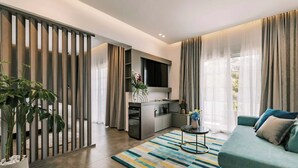 Una sala de estar moderna con un sofá, una mesa de centro y un televisor. Hay una zona de cocina con una mesa de comedor y sillas. La habitación tiene un ventanal con cortinas.