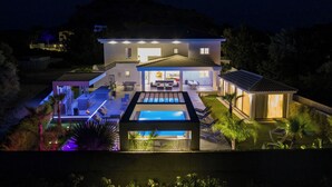 Una casa moderna con piscina, mobiliario exterior y un patio bien iluminado.