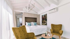 Un dormitorio moderno con una cama, dos sillas, una mesita y un ventanal grande.