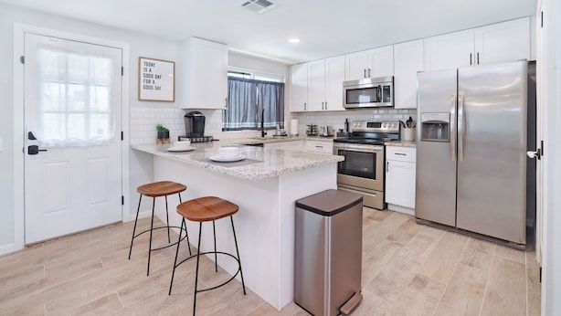 Una cocina moderna con armarios blancos, electrodomésticos de acero inoxidable y una isla central con taburetes.