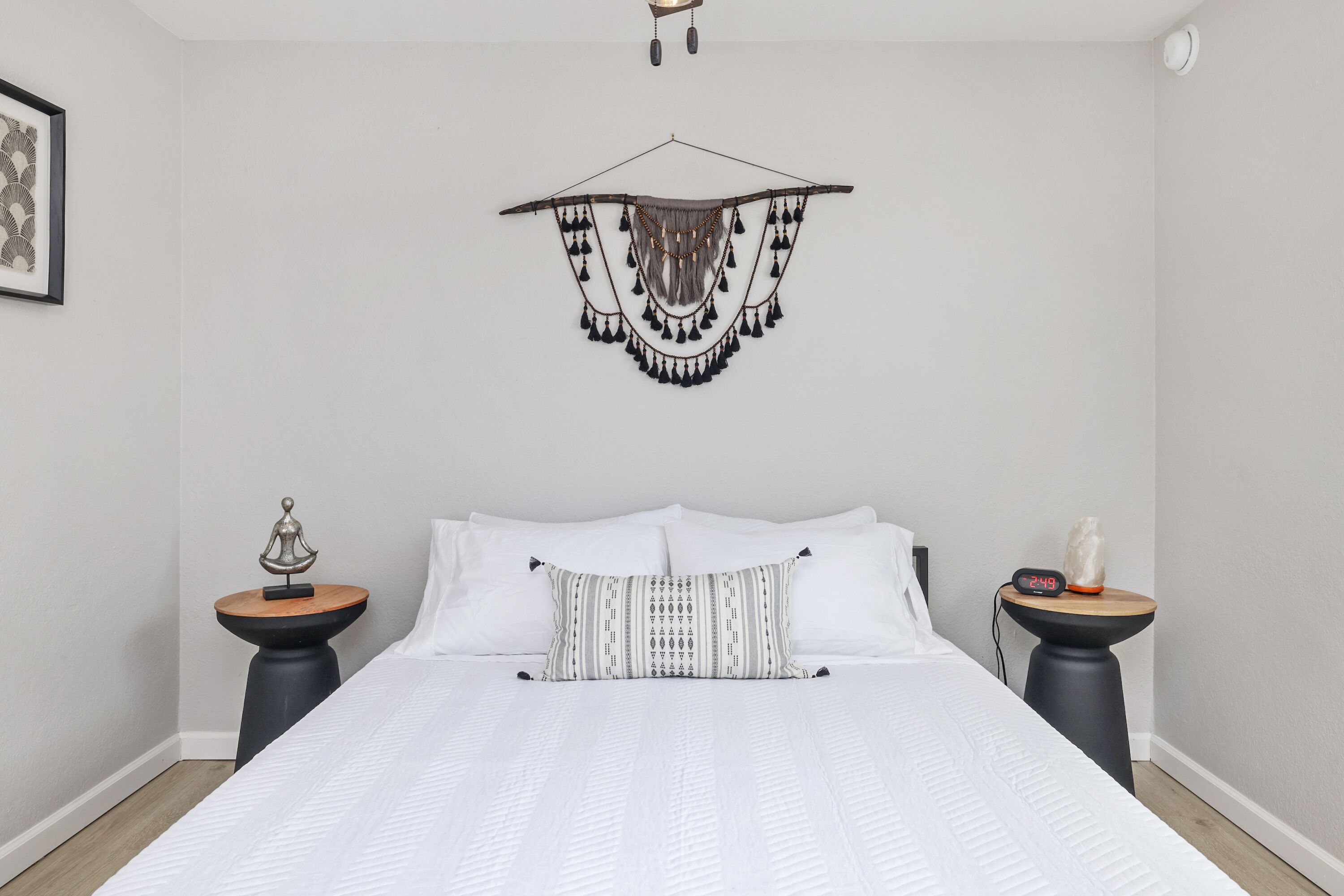 A neatly arranged bedroom with a large bed, two bedside tables, a wall-mounted hanging, and a framed picture.