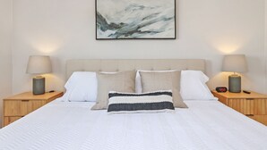 Un dormitorio ordenado con una cama grande, dos mesitas de noche y un cuadro abstracto colgado en la pared.