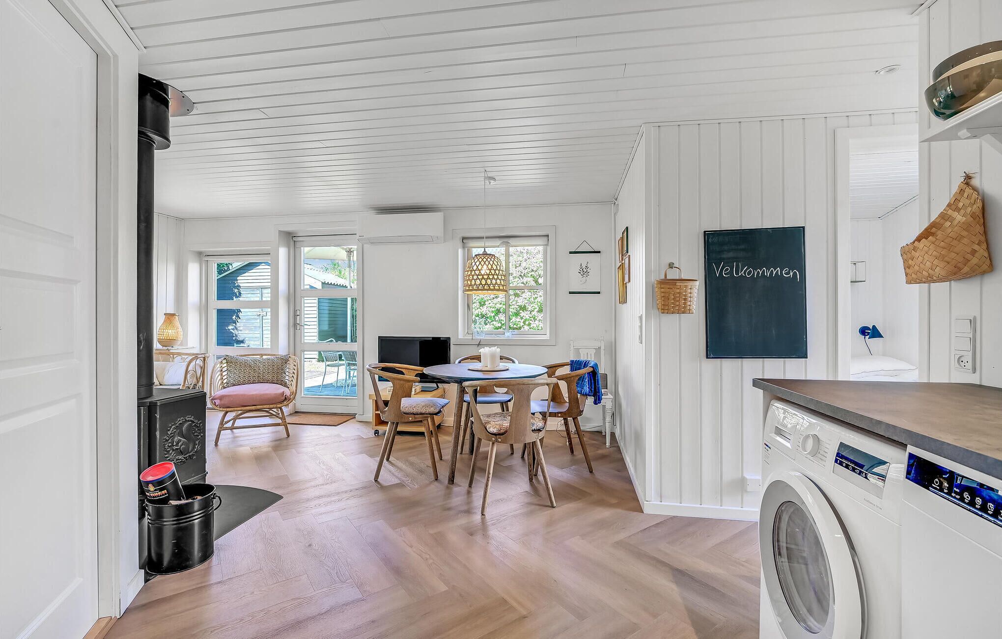 Une cuisine moderne dotée d’un lave-linge encastré, d’un plancher en bois et d’un coin repas avec des chaises en osier.