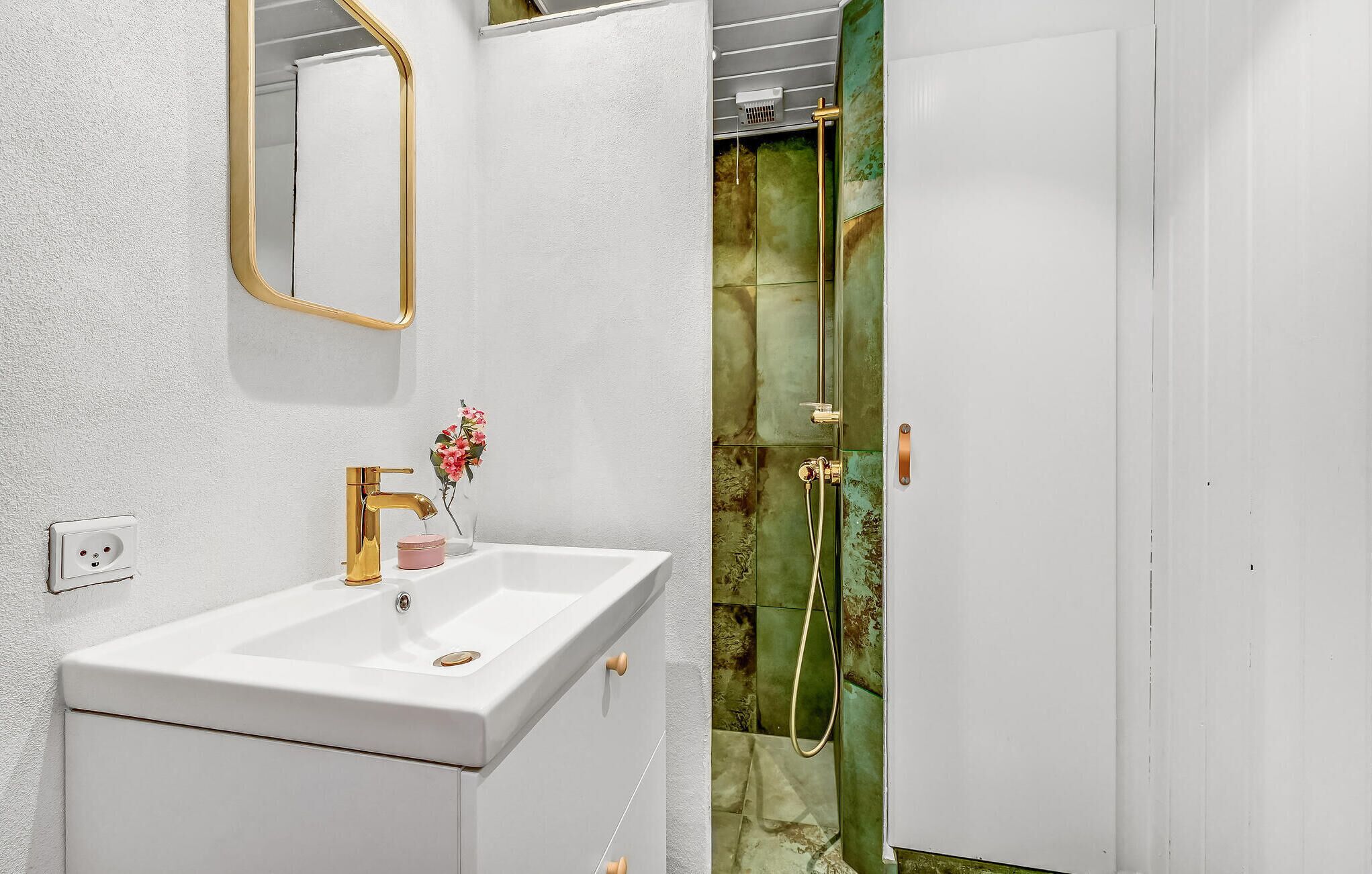 A bathroom with a white sink, gold faucet, and a mirror with a gold frame.