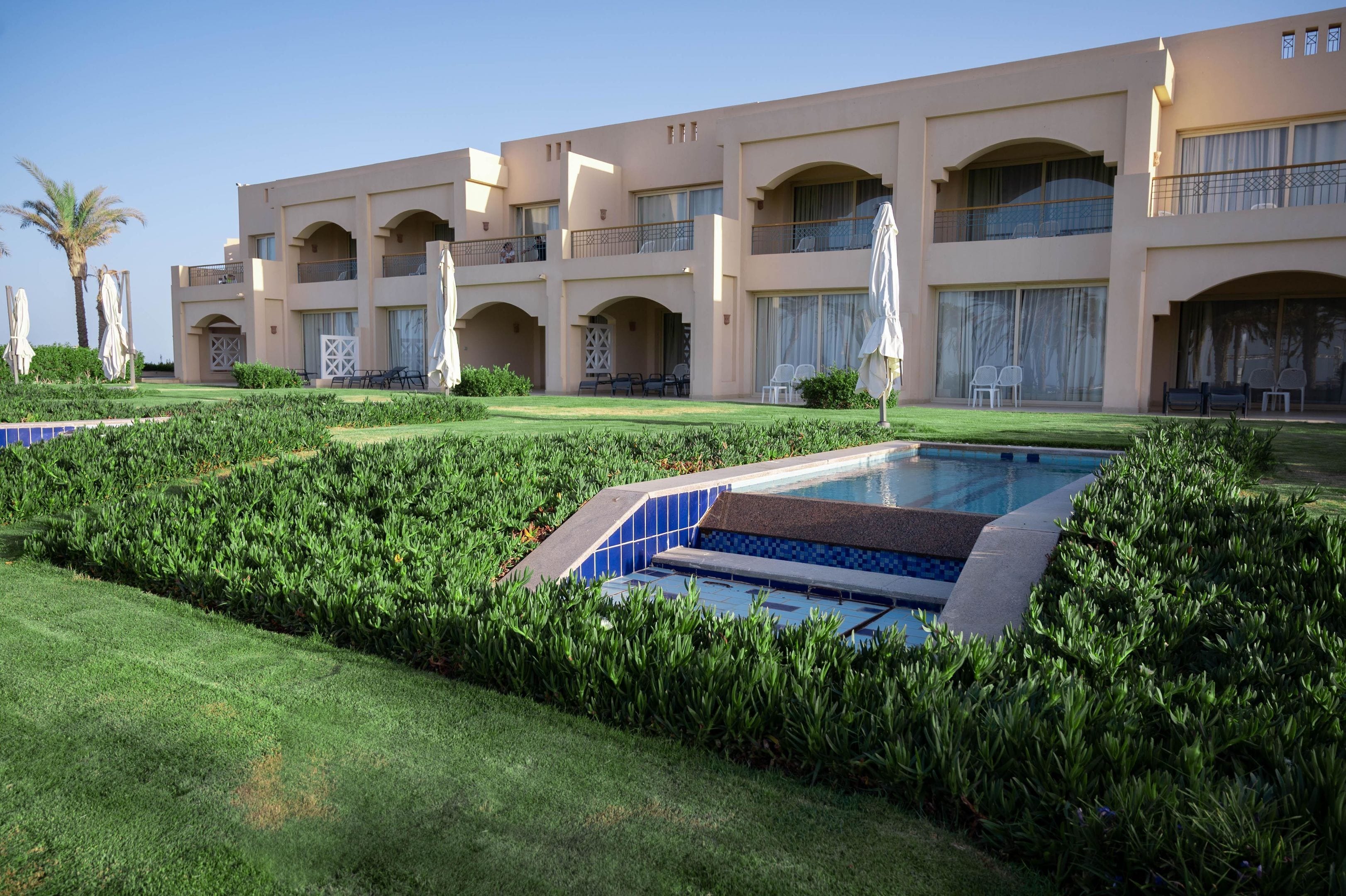A hotel with a pool, well-maintained lawn, and multiple balconies.