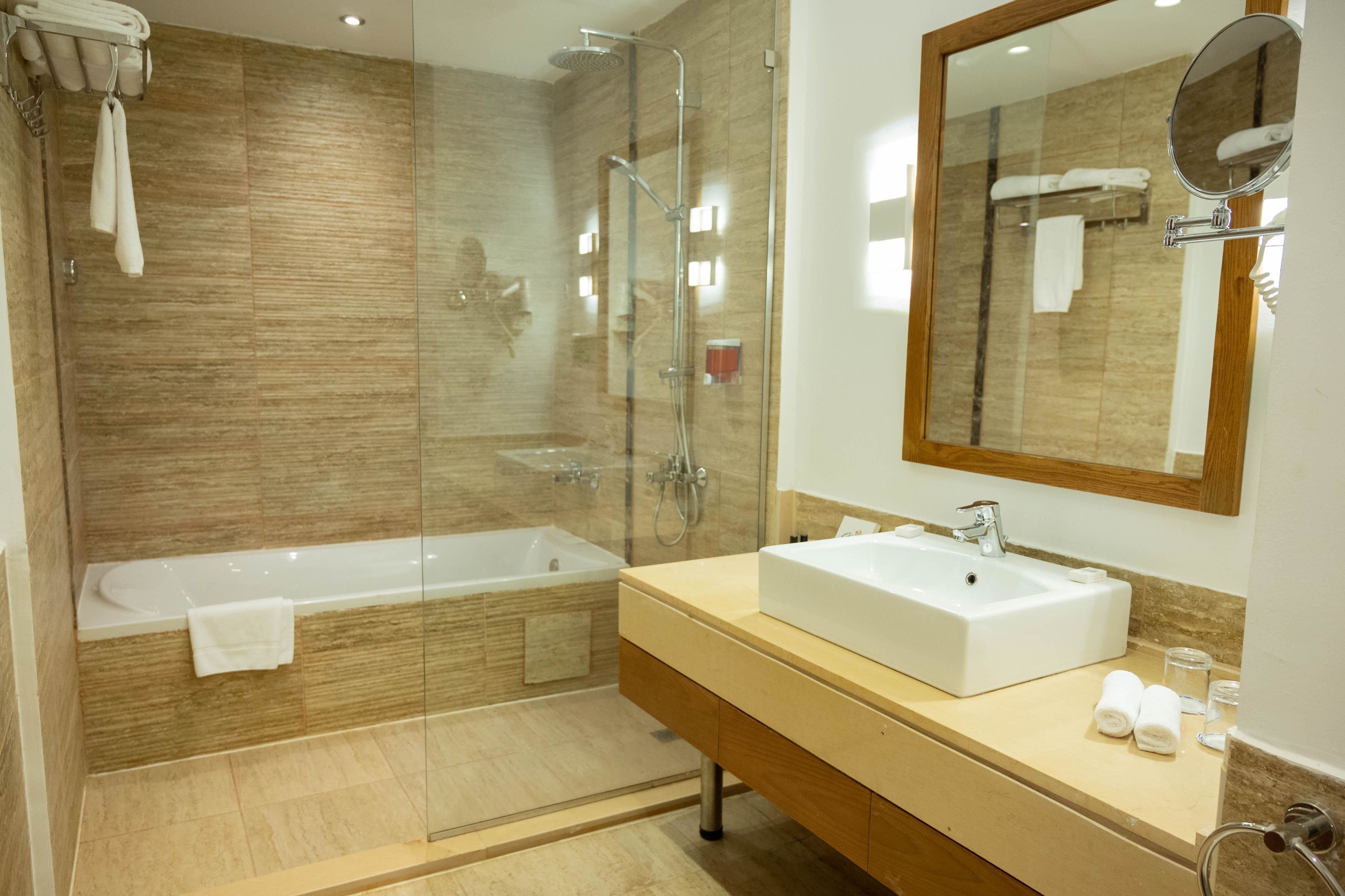 A modern bathroom with a glass-enclosed shower, a white bathtub, and a vanity with a large mirror.