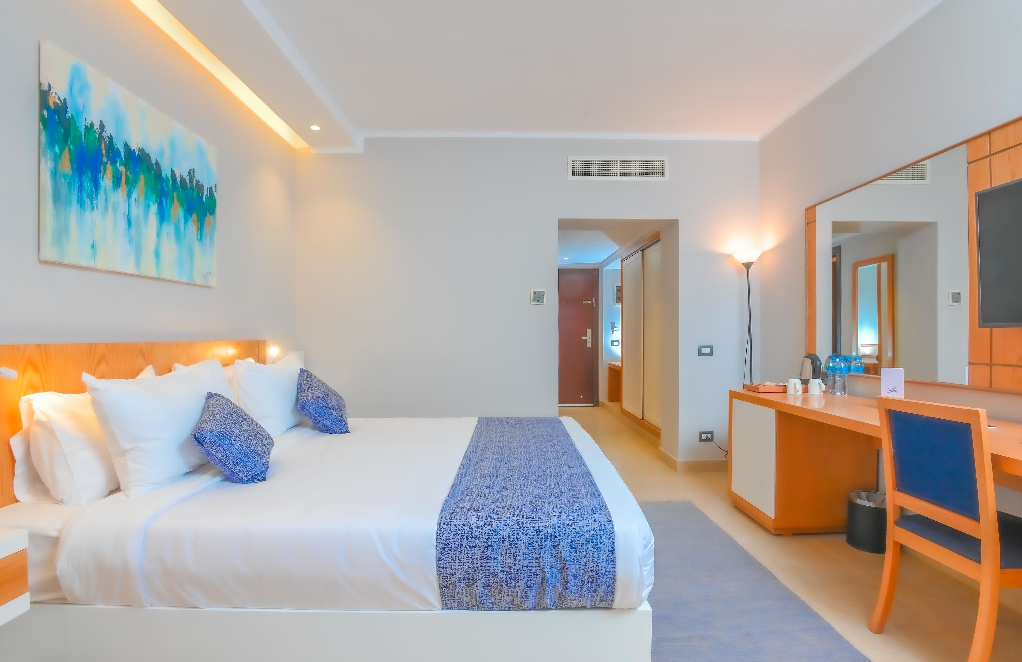 Een hotelkamer met een bed, een bureau, een stoel, een spiegel en een schilderij aan de muur.