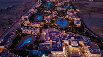 An aerial view of a resort with multiple swimming pools, beachfront villas, and a central courtyard.