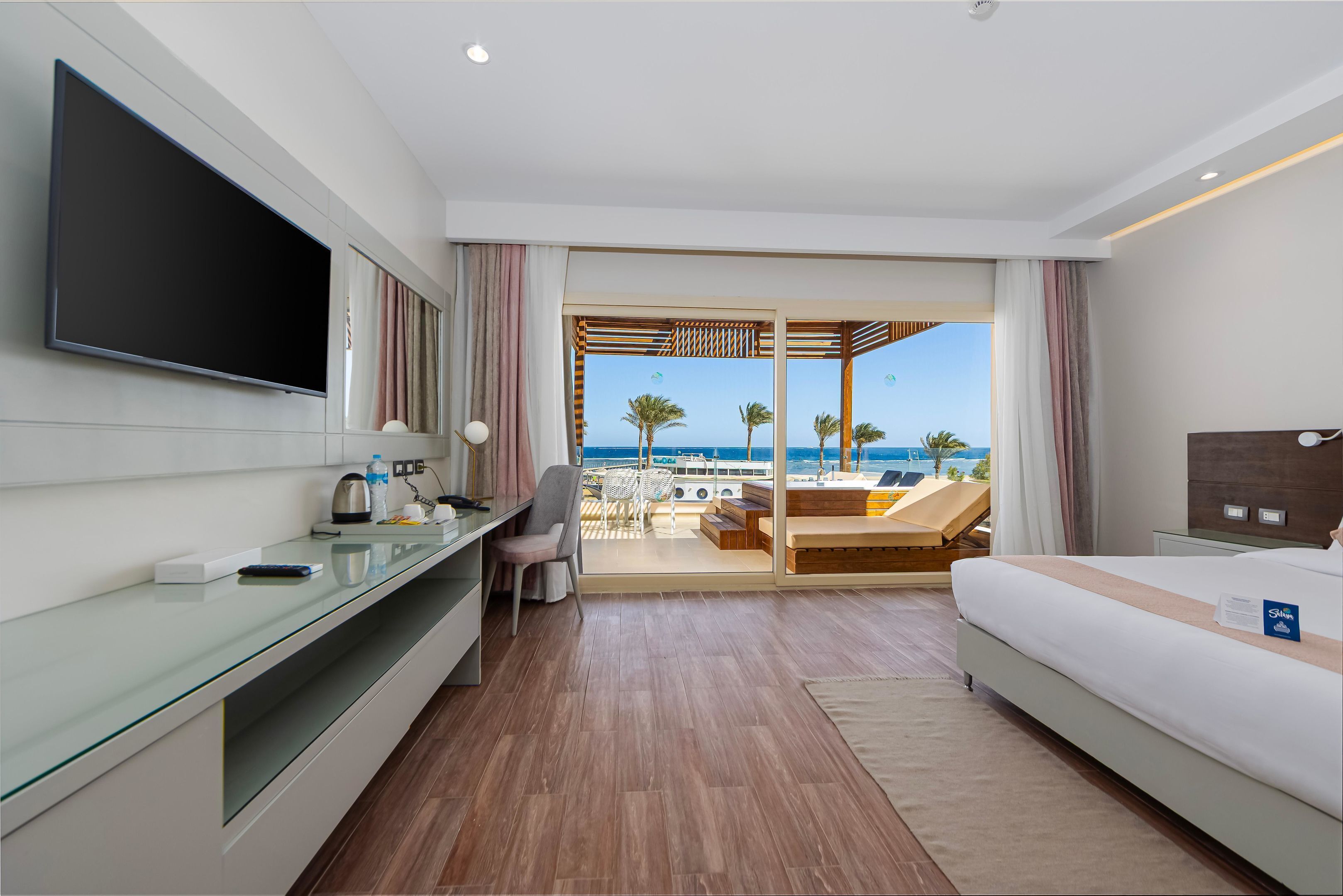 Ein Hotelzimmer mit großem Fernseher, Schreibtisch, Stuhl, Bett und Meerblick.