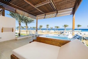Habitació amb sostre de fusta, un llit, vista a la platja i zona de piscina.