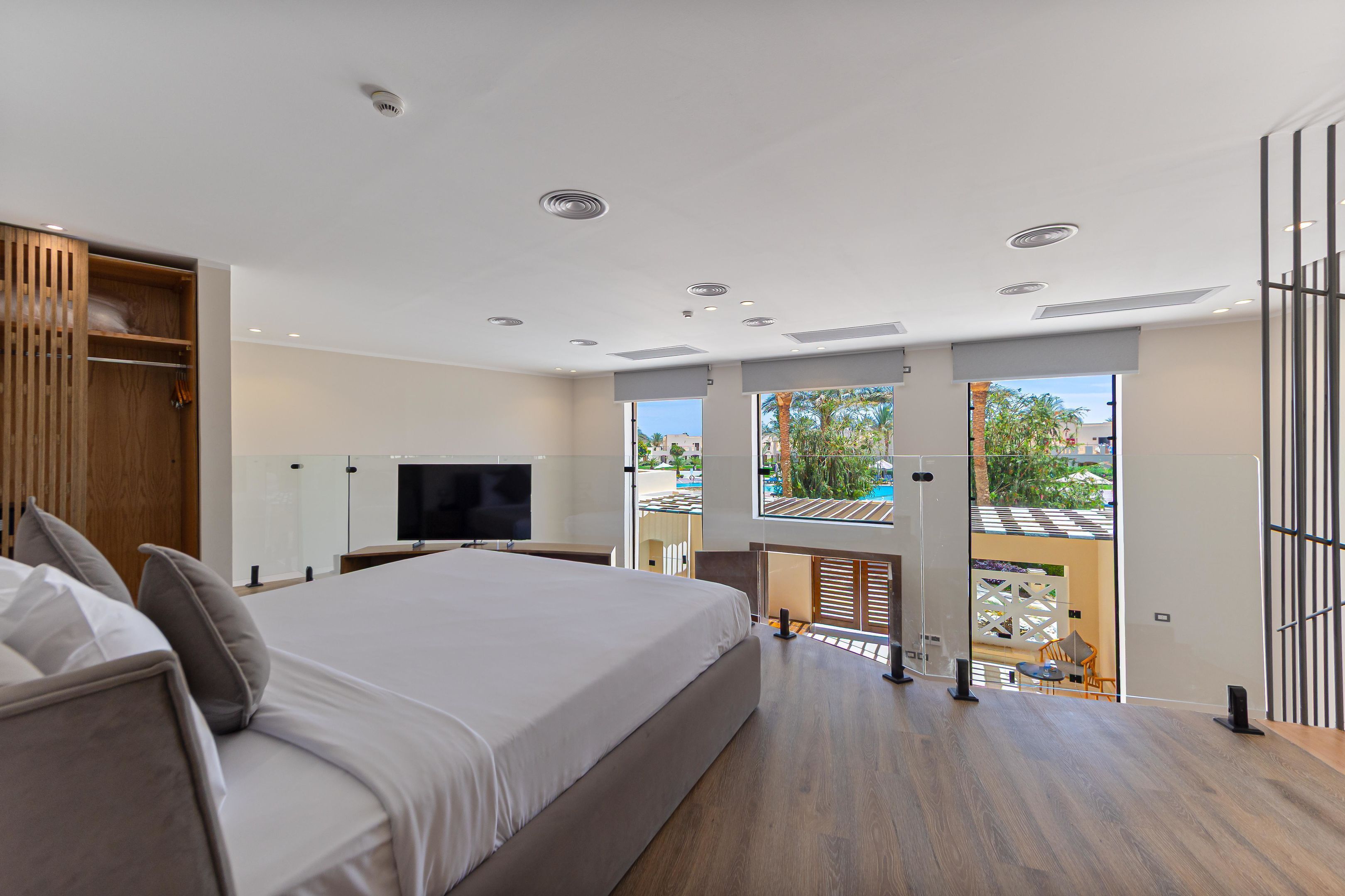 A modern bedroom with a large bed, a TV, and a balcony with a view.