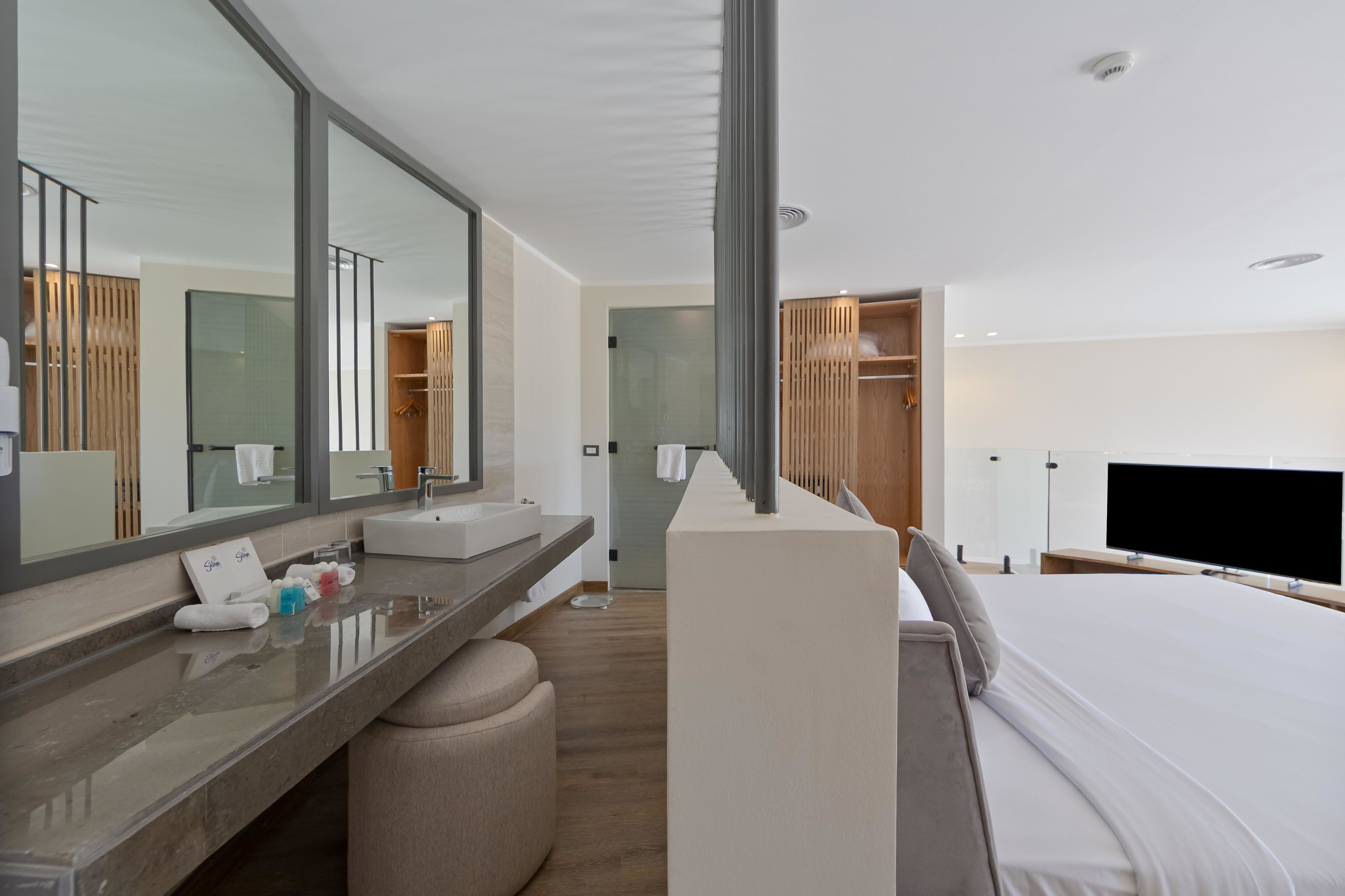 Een moderne hotelkamer met een groot bed, een kaptafel met spiegel, een flatscreen televisie en een inloopkast.