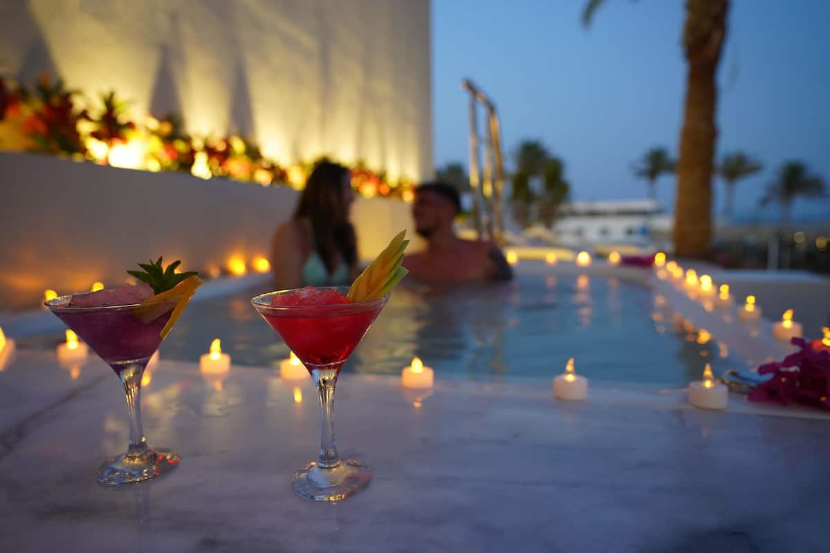 Two cocktails on a marble table with candles around a pool area.