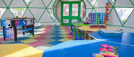 A room with a foosball table, colorful mats, and a table with books and toys.