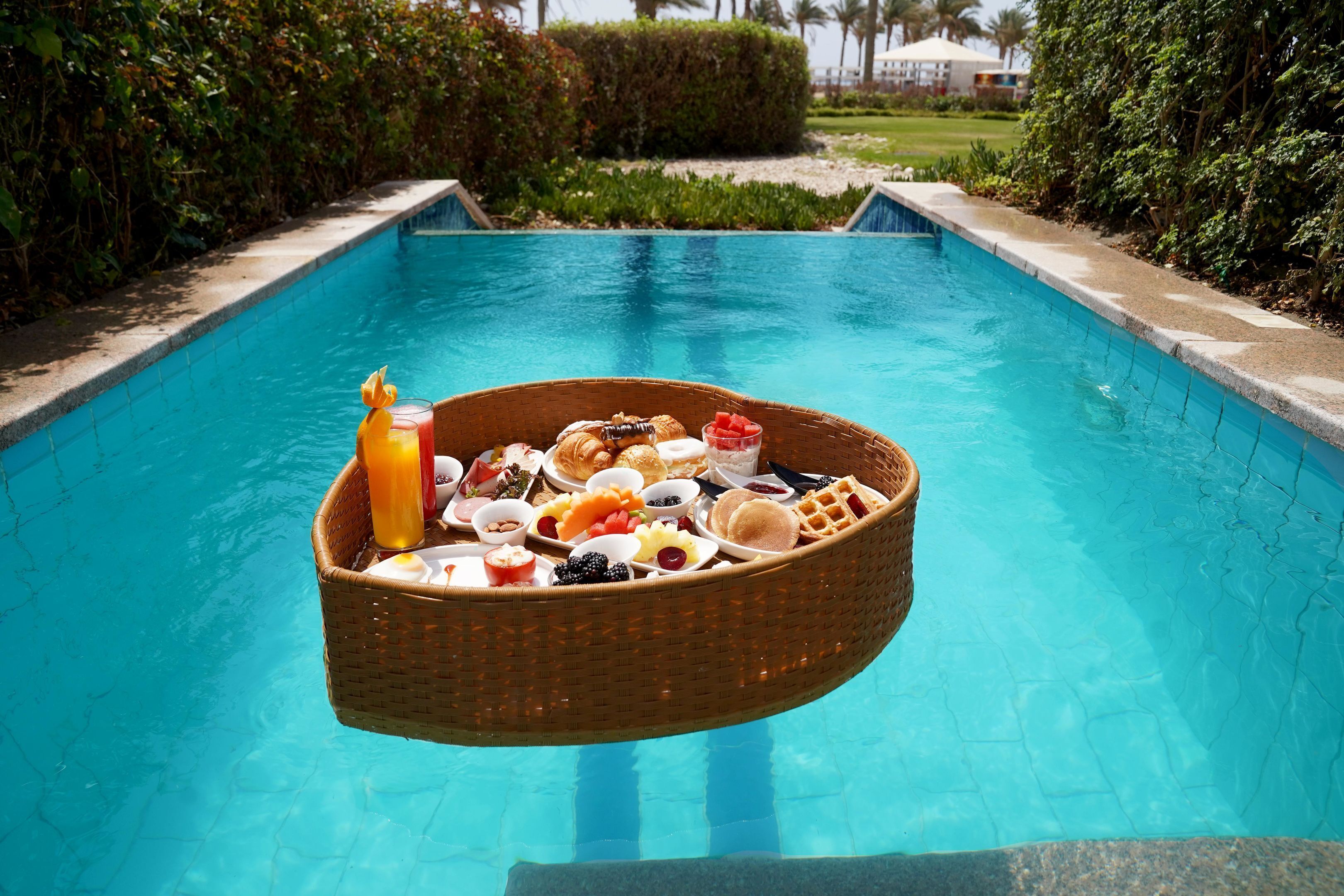 A floating basket with breakfast items over a pool.