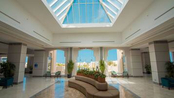 A spacious lobby with a high ceiling, a central curved sofa, and potted plants.
