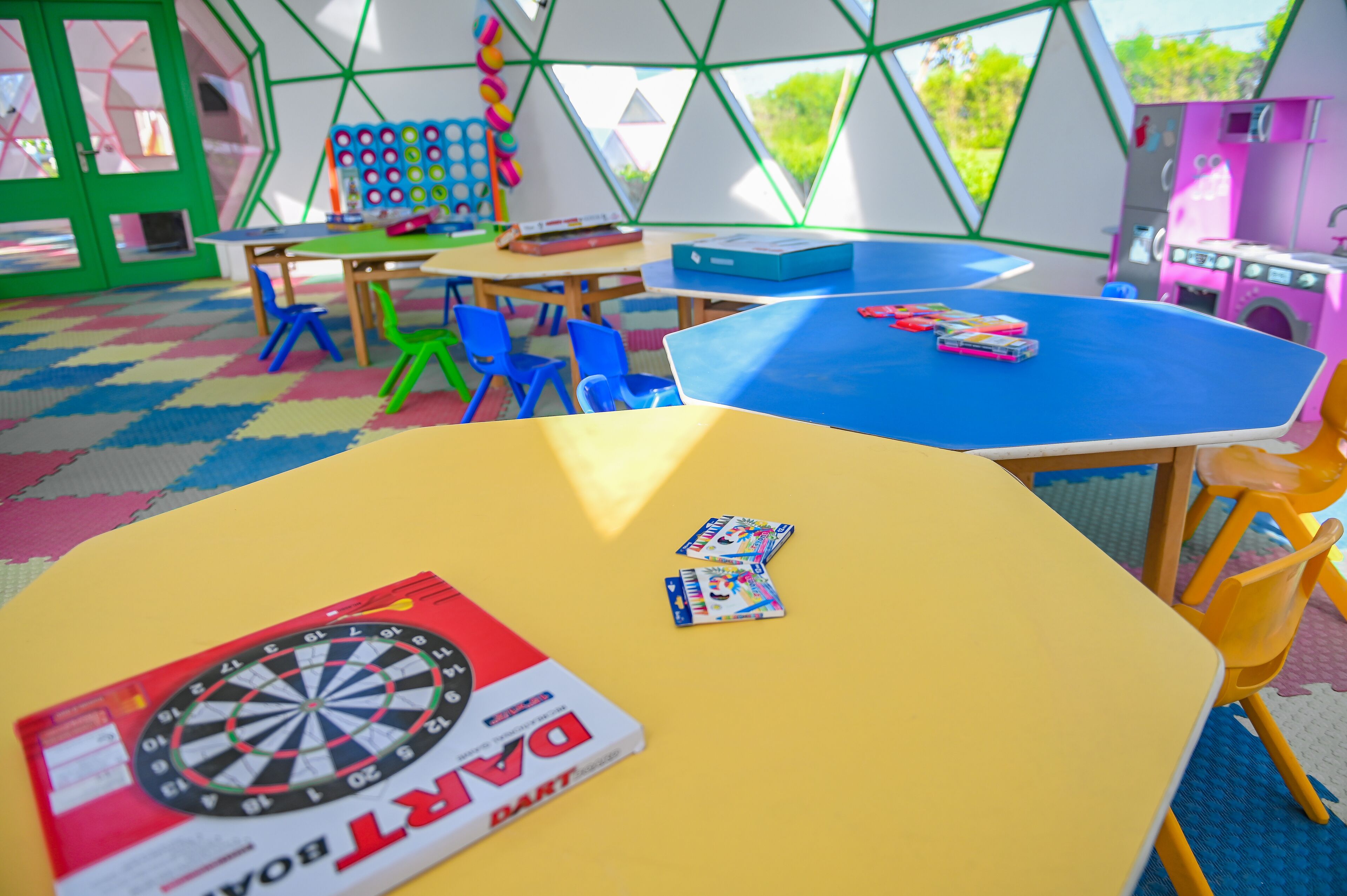 A colorful indoor play area with tables, chairs, and a dartboard.