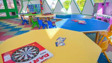 A colorful indoor play area with tables, chairs, and a dartboard.