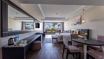 A modern hotel room with a large bed, a dining table, a seating area, and a view of the beach.