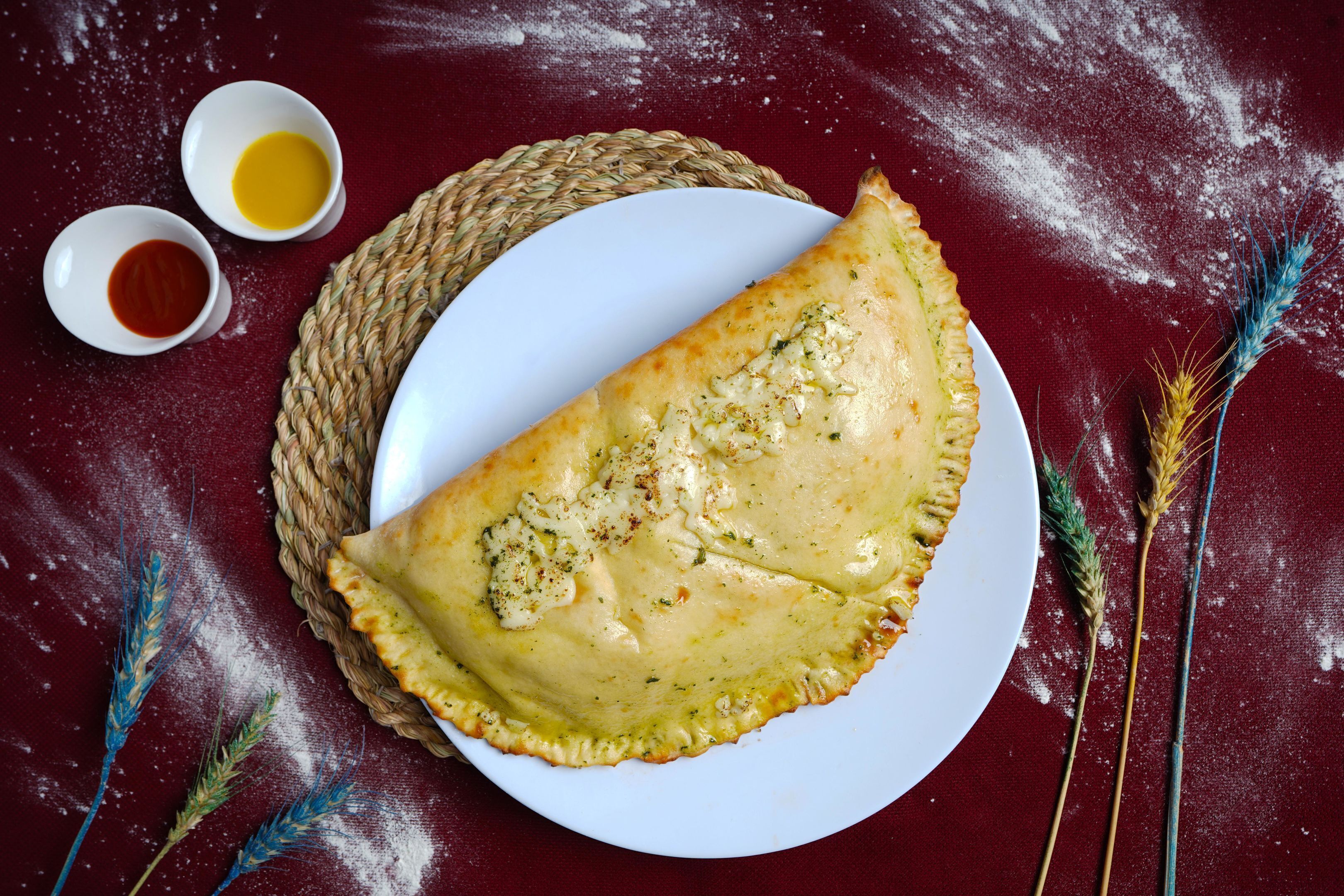 A folded pastry on a plate with two small bowls of sauces.