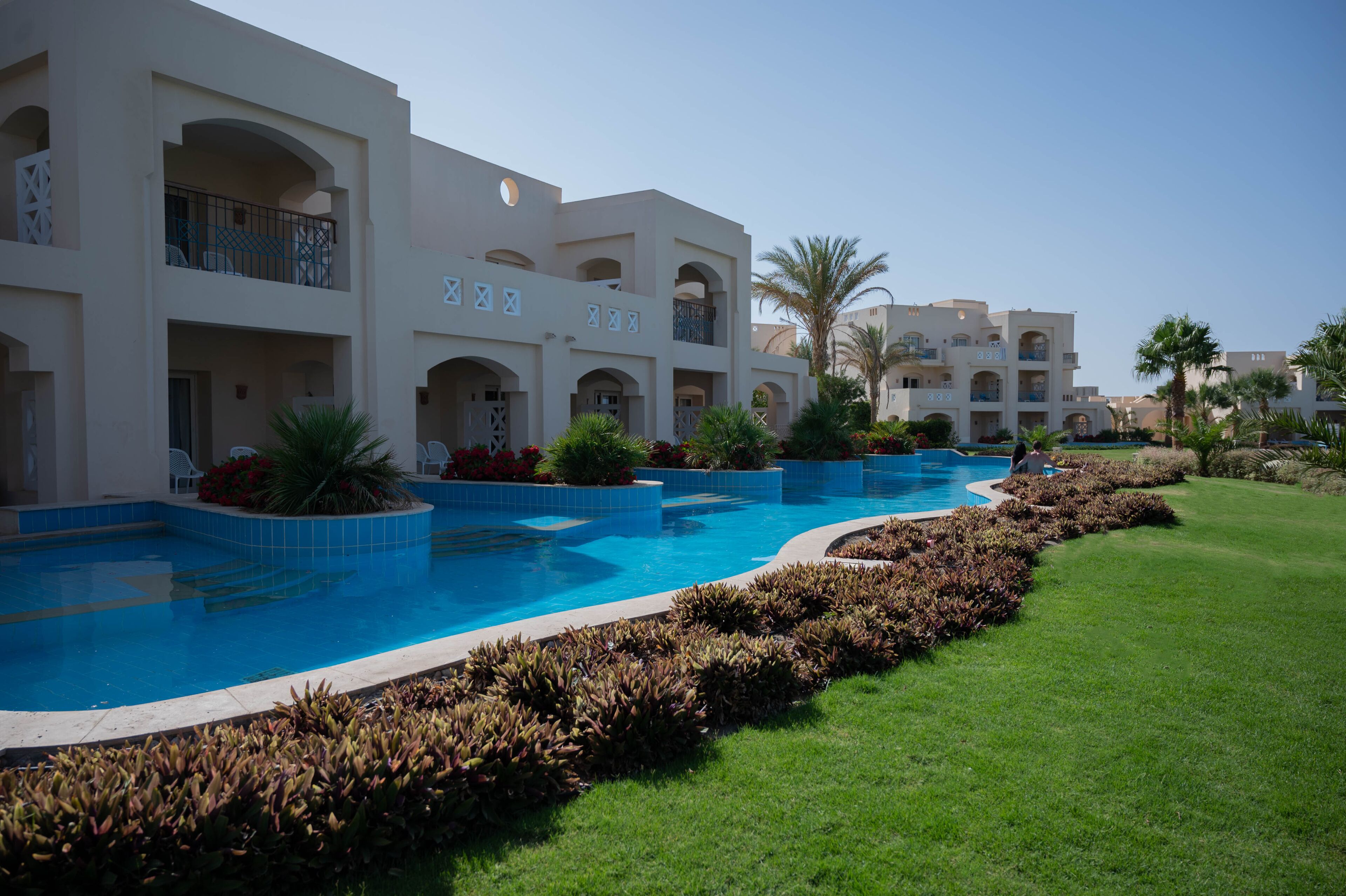 A hotel with a swimming pool, multiple balconies, and lush landscaping.