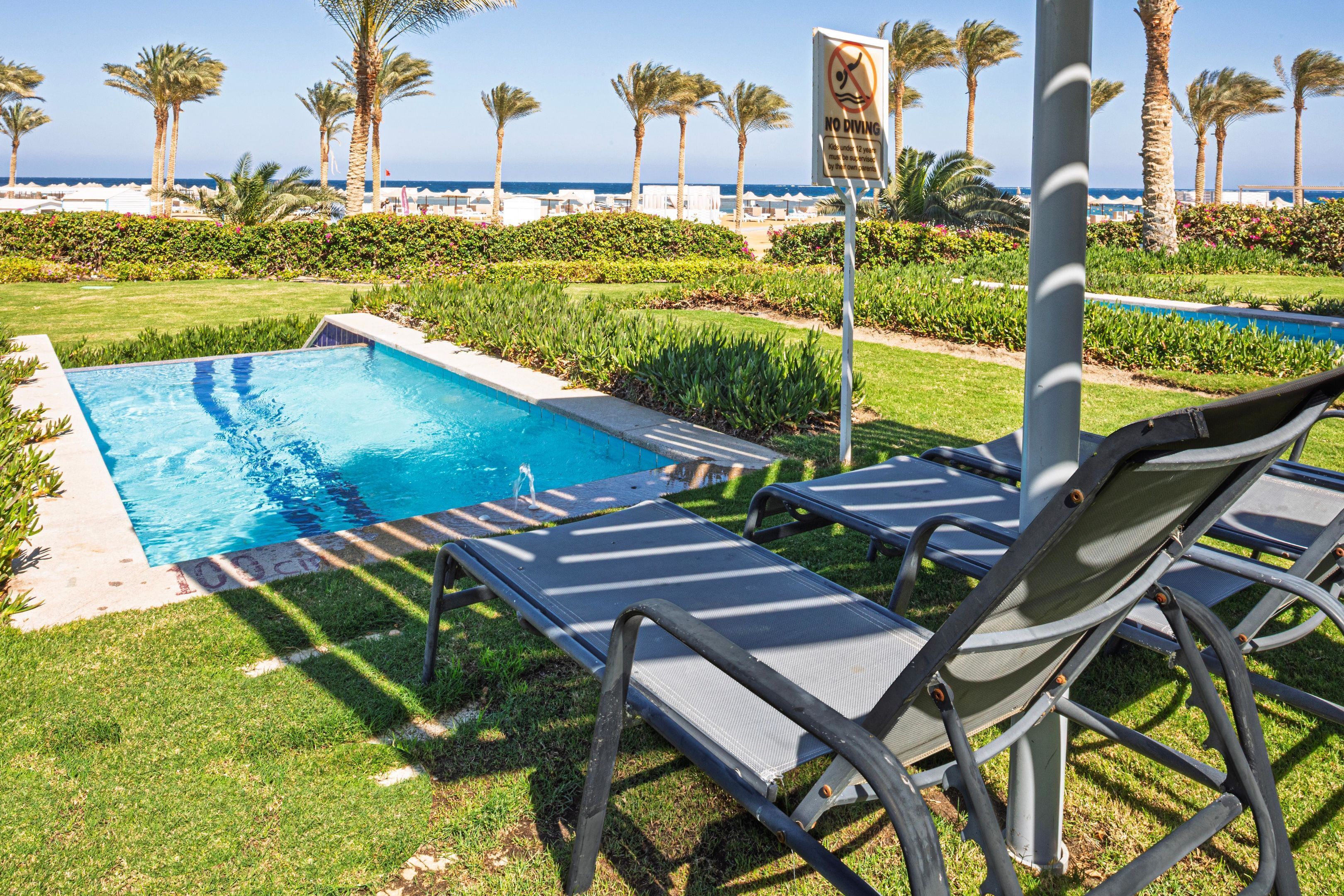 A pool area with lounge chairs, a 'No Diving' sign, and a view of the beach and ocean.