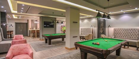A pool table with a green felt surface, a seating area with cushioned chairs, and a bar area with stools.