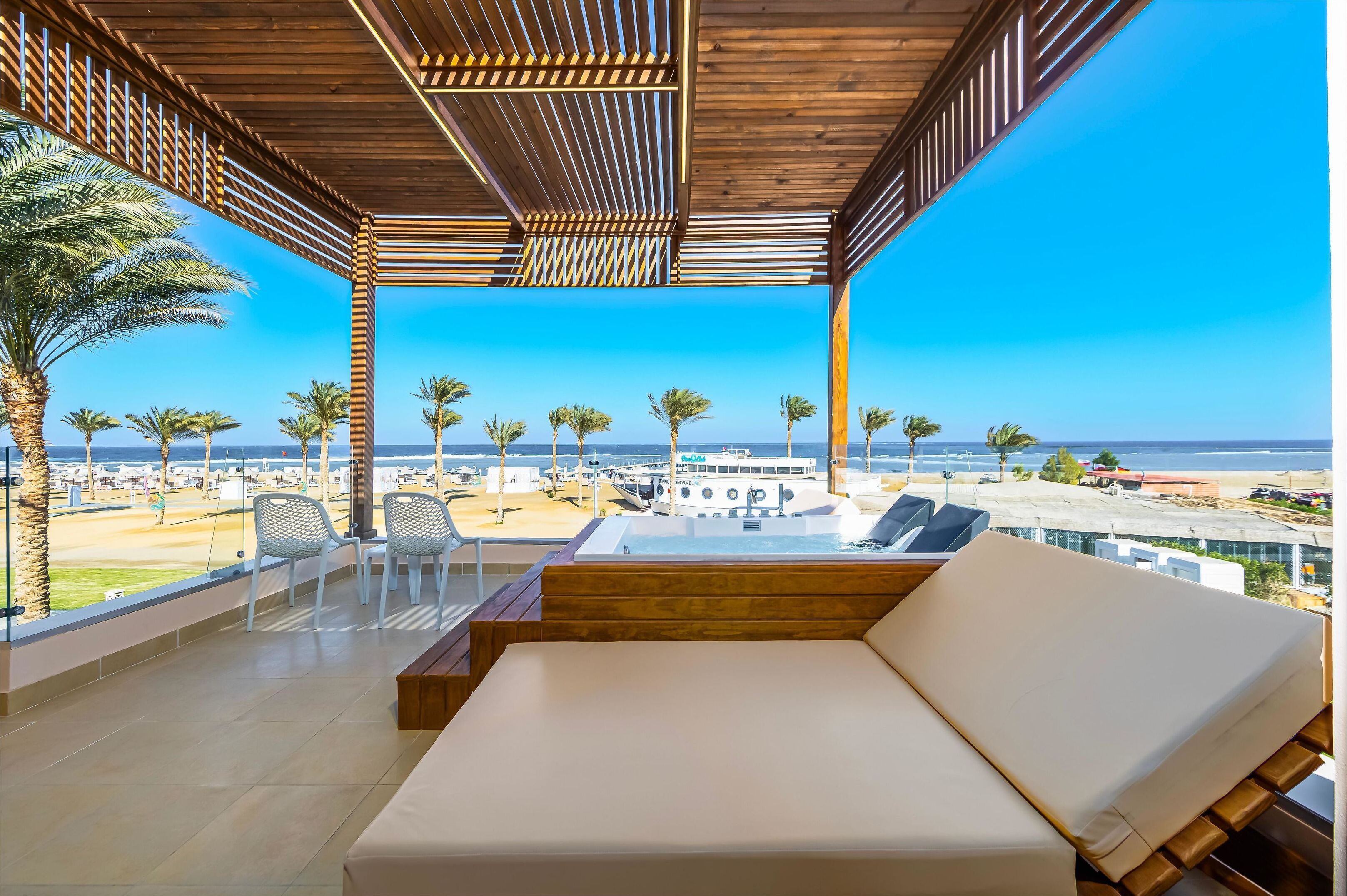 Un salon extérieur moderne doté d’un plafond en bois, de sièges blancs rembourrés et offrant une vue sur la plage et l’océan.