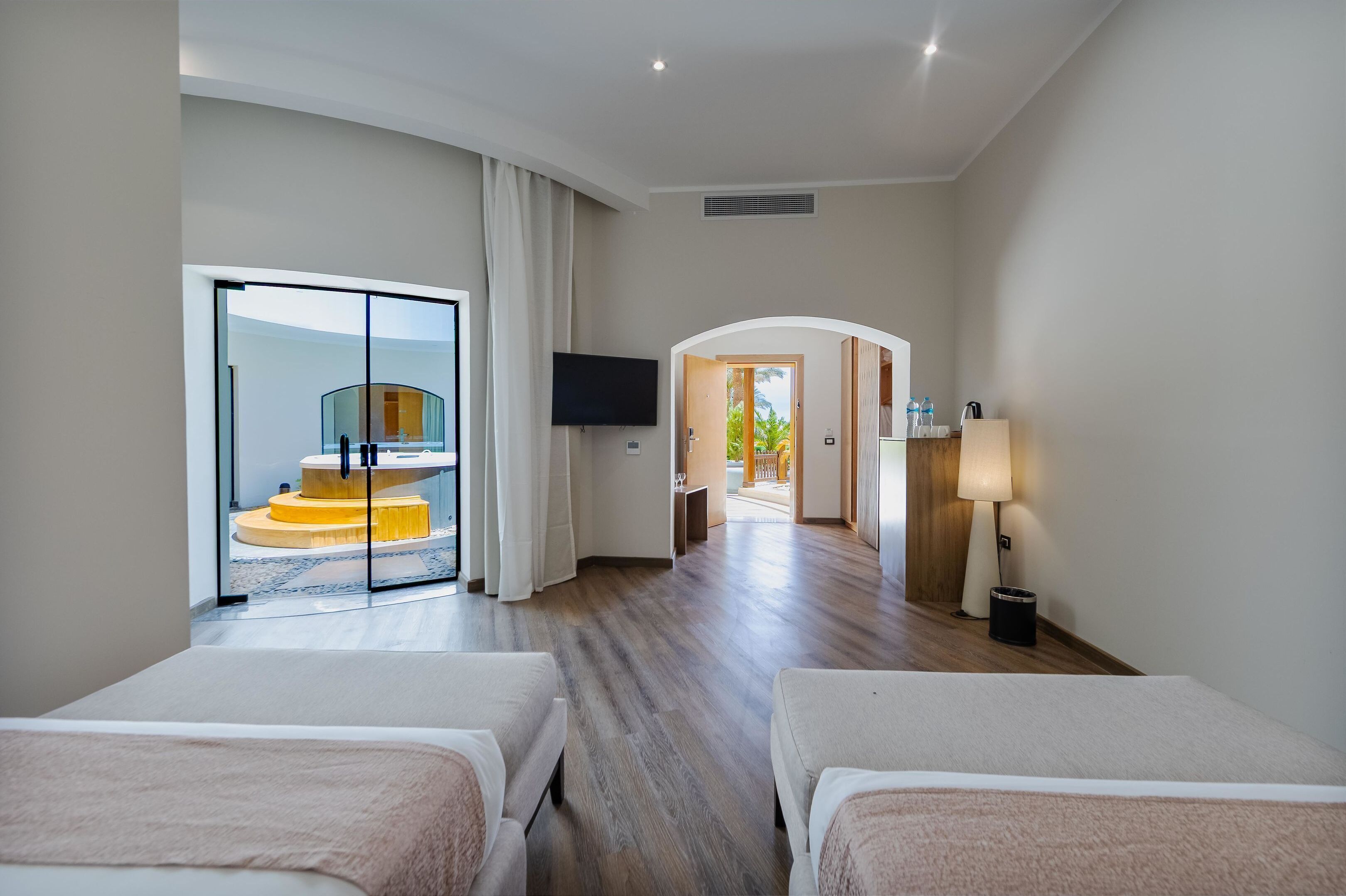 A hotel room with two beds, a TV, a lamp, and a view of a spiral staircase.