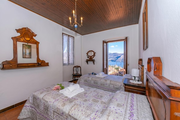 A bedroom with two beds, a wooden ceiling, a chandelier, a large mirror, and a view of mountains.